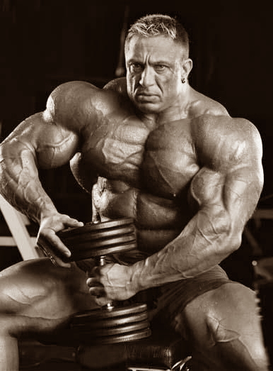 A powerful bodybuilder sitting with intense focus, showcasing muscular definition and strength.
